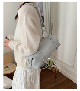 Light blue-grey cylindrical shoulder bag with matte leather texture in a cozy home setting