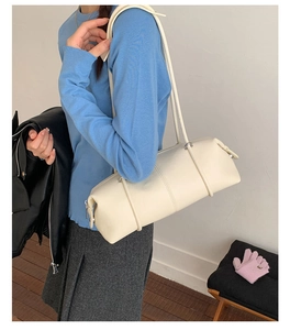 Side view of cream white cylindrical leather shoulder bag with a long strap