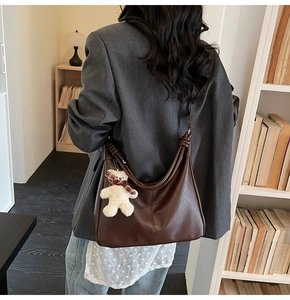 Brown leather crescent tote bag with knotted strap and white plush bear charm on model