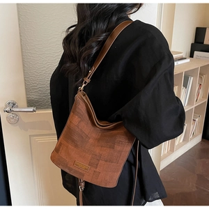 Vue détaillée de la texture du sac seau marron et de la plaque logo en métal sur cuir