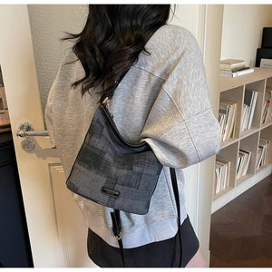 Détail du sac seau en tissu gris avec bandoulière en cuir noir et plaque logo dorée