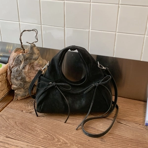 Detail shot of black suede cloud bag featuring decorative bows and round handle on wood