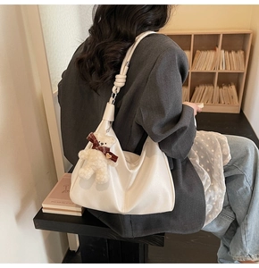 Detail of white half-moon tote bag with soft leather pleats and plush bear charm