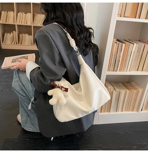 Detailed view of white hobo tote bag with knot shoulder strap and plush bear charm