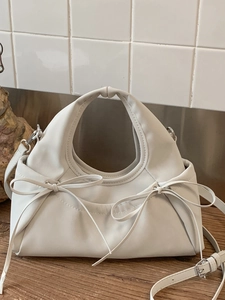Chic beige bow ruched cloud handbag with ring handle and adjustable strap on wood