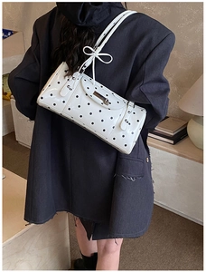 Sac sous le bras à pois avec rivets argentés et nœud, porté par un mannequin élégant