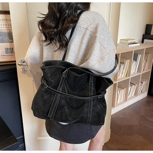 Detail shot of black tote bag with white contrast stitching on model in a cozy room