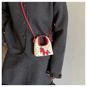 Close-up of a mini cream handbag with red polka dots and horse embroidery detail