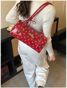 Sac à bandoulière rouge à pois blancs avec détail cœur doré porté par un mannequin