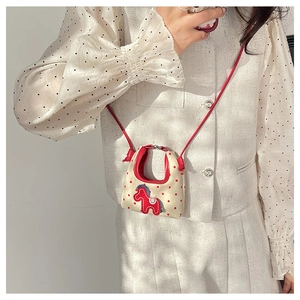 Detail of mini canvas crossbody bag with red polka dots and horse patch on a model
