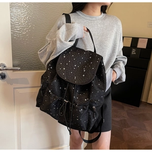 Detail view of black backpack with white star patterns featuring drawstring and flap closure