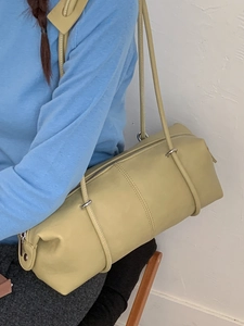 Minimalist pale yellow leather cylindrical tote bag with slim shoulder straps on model