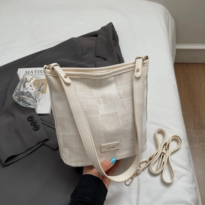 Détail d'un sac seau beige avec texture en toile, bordures en cuir et logo métallique
