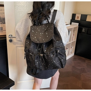 Detail of black backpack with white star print featuring drawstring and side zipper pocket
