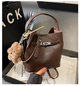 Detail of dark brown lychee leather bucket bag with metal lock and bear charm accessory