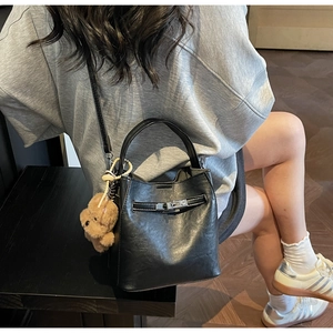 Side view of black faux leather bucket bag featuring a metal buckle and plush bear charm