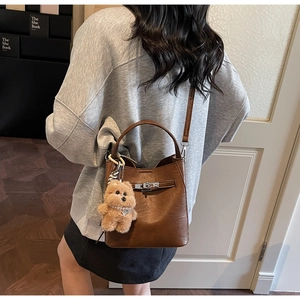Brown vintage leather bucket bag featuring metal lock closure and cute plush bear charm