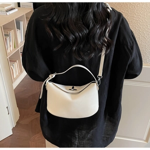 Close-up of a white minimalist half-moon bag with a metal twist-lock and wide handle
