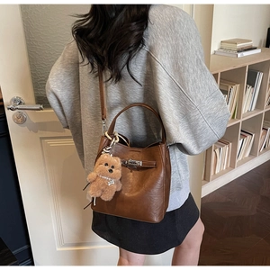 Detail of dark brown leather bucket bag with silver twist lock and plush bear pendant