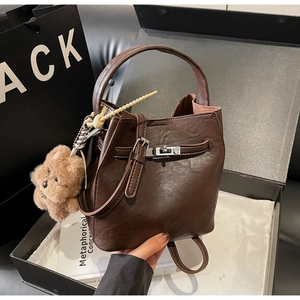 Brown leather bucket bag inside a premium gift box with plush bear charm detail