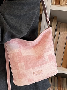 Sac seau texturé rose et beige avec garniture en cuir porté par un mannequin près d'une étagère