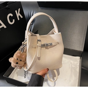 Detail view of cream bucket bag with textured leather, metallic buckle, and plush bear charm