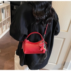 Détail d'un petit sac carré rouge avec pendentif cheval et bandoulière chic