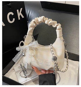 Detail of white pleated handbag with bear embroidery, lace bow, and pearl charms