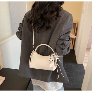 Gros plan du sac demi-lune crème avec breloque cheval porté sur un blazer gris