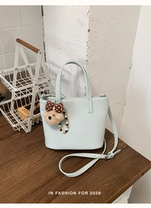 Detail of mint blue leather tote bag with cute plush bear charm on a wooden table
