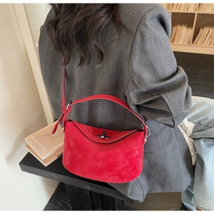 Modèle portant un sac à main rouge style Boston à l'épaule avec un costume gris foncé