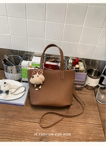 Close-up of brown lychee grain tote bag with cute plush bear charm on wooden table