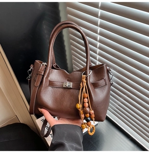 Detail view of a dark brown handbag with wooden bead pendant and elegant metal buckle