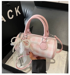 Detail of pink plaid cylinder bag with pearl lace bow charm and adjustable strap