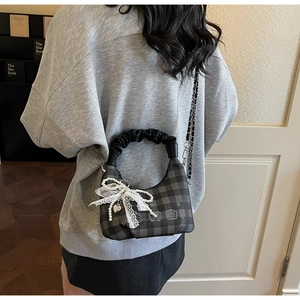 Detail of checkered hobo bag with lace bow pendant and pearl strap on model