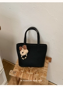 Detail view of black lychee grain tote bag with a cute brown plush bear charm