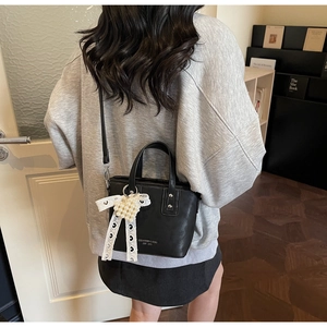 Dettaglio di una borsa a secchiello nera con fiocco di pizzo e ciondolo di perle