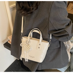 Dettaglio di una borsa a secchiello bianco crema con ciondolo a perla e pizzo bianco
