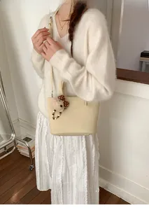Close-up of creamy white faux leather tote bag with cute brown polka dot bear charm