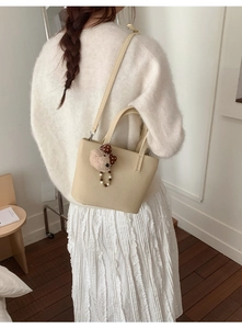 Chic beige bucket bag shown on model's shoulder with cute plush bear charm detail