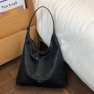 Dettaglio di una borsa tote nera capiente con mini pochette coordinata su un letto bianco
