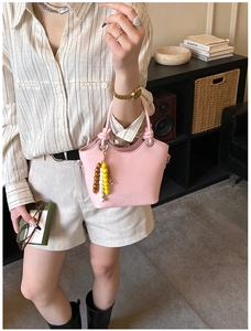 Sac seau rose avec texture cuir et poignée en perles de bois colorées sur un mannequin
