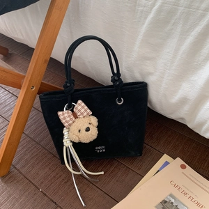 Detail of black tote bag featuring rope handles and a plush bear charm with plaid bow