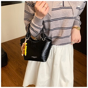 Détail d'un sac seau en cuir verni noir avec breloque perlée et lettrage imprimé