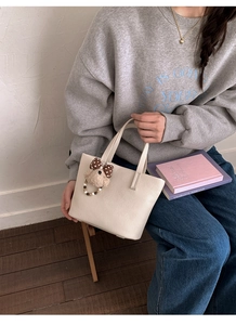 Detail view of cream bucket bag in pebble leather with a cute plush bear charm