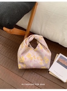 Detail einer floralen Satin-Handtasche mit Knotengriff auf warmem Holzhintergrund
