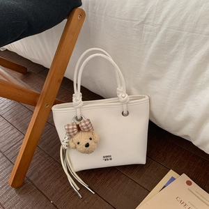 Detail of white leather bucket bag with knotted handles and a cute teddy bear charm