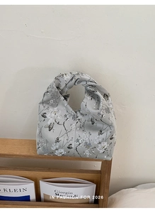 Detail einer grauen Knotentasche mit Pflaumenblüten-Print auf einem Holzständer