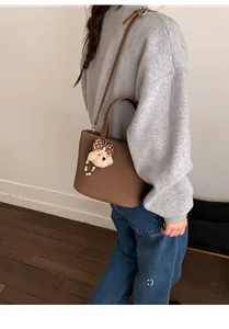 Detail of a brown leather tote bag with a cute teddy bear charm and adjustable strap
