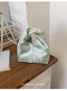 Detail einer mintgrünen floralen Satin-Handtasche mit elegantem Knotengriff und Seidenglanz
